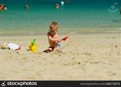 Toddler boy playing with shovel and sand on beach . Two year old toddler boy playing with shovel and sand on beach