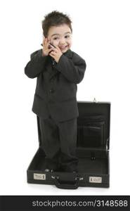 Toddler boy standing in empty briefcase talking on cellphone. Wearing suit and tie. Shot in studio over white.
