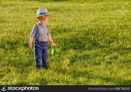 Toddler child outdoors. One year old baby boy wearing straw hat using watering can. Portrait of toddler child outdoors. Rural scene with one year old baby boy wearing straw hat using watering can