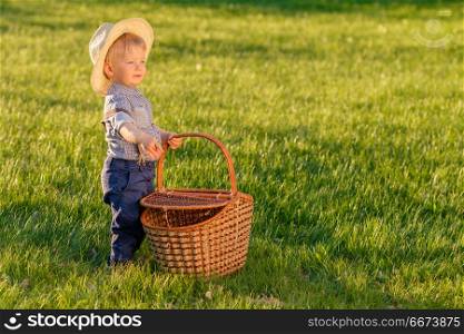 Toddler child outdoors. One year old baby boy wearing straw hat with picnic basket. Portrait of toddler child outdoors. Rural scene with one year old baby boy wearing straw hat and picnic basket