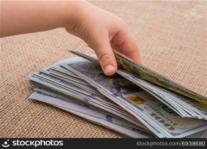 Toddler hand holding banknote bundle of US dollar on a linen canvas background