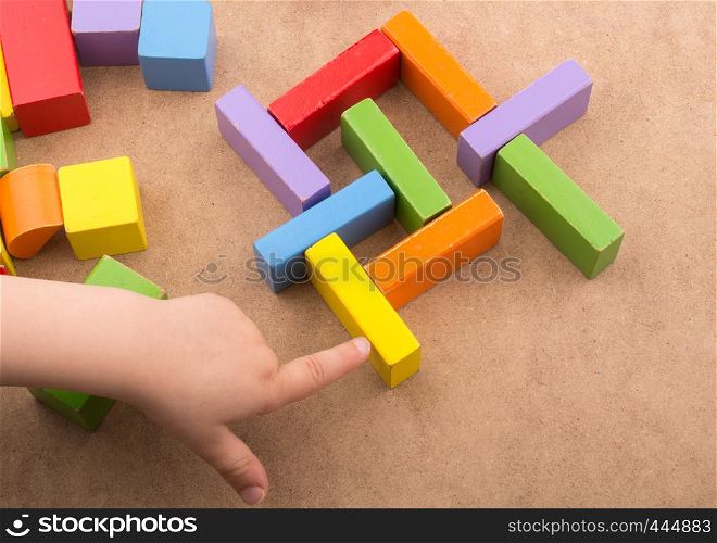 Toddler hand over Colorful building blocks on brown background