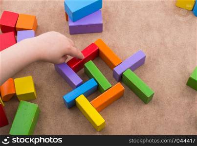 Toddler hand over Colorful building blocks on brown background