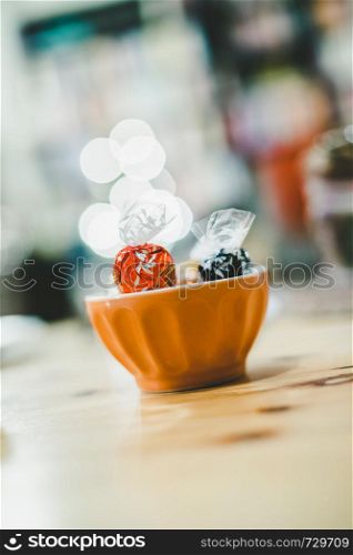 Toffees in a ceramic bowl on a wooden desk, blurry background. Christmas.