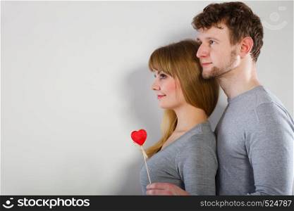 Togetherness in love. Attractive young smiling couple with little red heart on stick. Woman and man having good relationship.. Charming young pare with little heart.