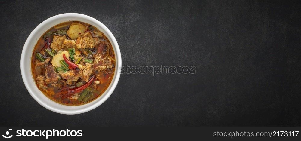 Tom Yum, Thai food, hot, spicy and sour stewed beef soup in bowl on dark gray, grey, black tone texture background with copy space for text, 64 x 27 ultra widescreen aspect ratio