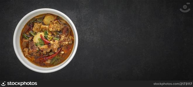 Tom Yum, Thai food, hot, spicy and sour stewed beef soup in bowl on dark gray, grey, black tone texture background with copy space for text, 64 x 27 ultra widescreen aspect ratio