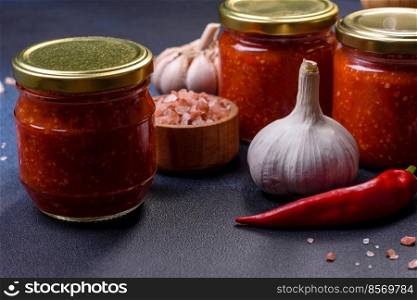 Tomato and chili sauce, jam, confiture in a glass jar on a blue stone background. Homemade hot tomato sauce adjika in jars. Tomatoes, chilli pepper, garlic and herbs