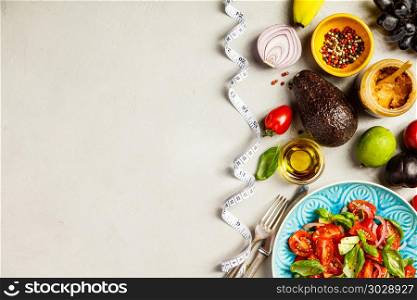 Tomato, basil, avocado and onion salad in blue plate for vegan, gluten free, allergy-friendly, clean eating or raw diet. Grey concrete background and top view. Healthy food and tape measure. Healthy food and tape measure