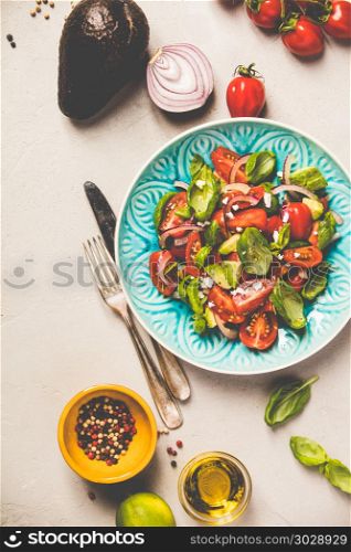 Tomato, basil, avocado and onion salad in blue plate for vegan, gluten free, allergy-friendly, clean eating or raw diet. Grey concrete background and top view. Healthy salad and ingredients. Healthy salad and ingredients