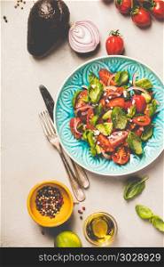 Tomato, basil, avocado and onion salad in blue plate for vegan, gluten free, allergy-friendly, clean eating or raw diet. Grey concrete background and top view. Healthy salad and ingredients. Healthy salad and ingredients
