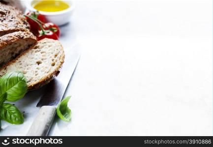 Tomato, bread, basil and olive oil on white marble background. Italian cooking, healthy food or vegetarian concept