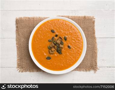 Tomato cream soup with pumpkin seeds and crackers on a wooden background