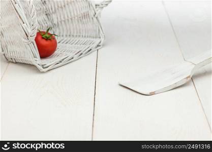 tomato in a wicker basket and a wooden spoon on a white old wooden boards. tomato in a wicker basket and a wooden spoon