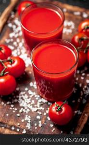 Tomato juice in a glass with pieces of salt. On a wooden background. High quality photo. Tomato juice in a glass with pieces of salt.