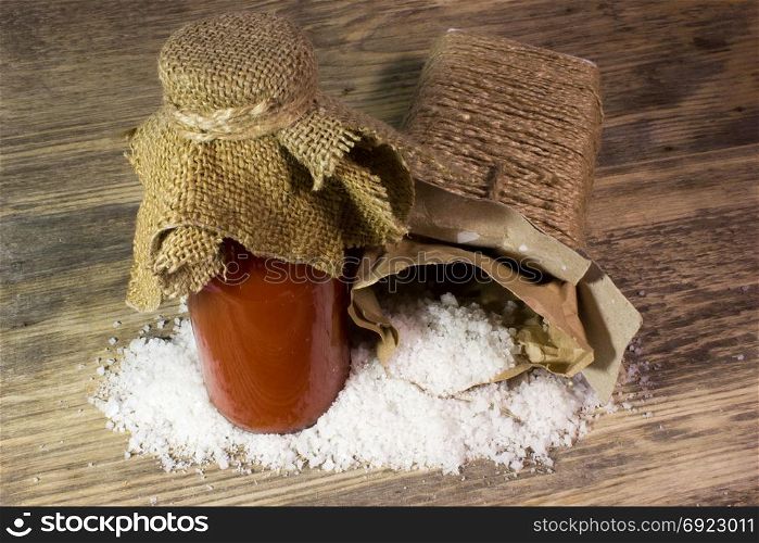 Tomato juice in glass bottle and big sea salt on wooden background
