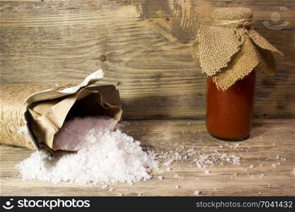 Tomato juice in glass bottle and big sea salt on wooden background