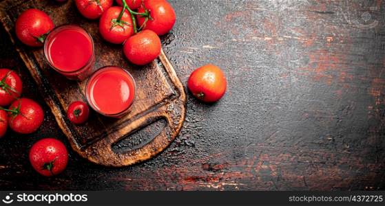 Tomato juice in glasses on a wooden cutting board. On a rustic dark background. High quality photo. Tomato juice in glasses on a wooden cutting board.