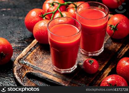 Tomato juice in glasses on a wooden cutting board. On a rustic dark background. High quality photo. Tomato juice in glasses on a wooden cutting board.