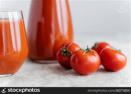Tomato juice in two glass cups and small ripe red tomatoes on white background. Fresh beverage containing vitamins. Healthy food