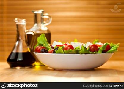 Tomato, mozzarella, or fetta cheese salad with black olives, olive oil and balsamic vinegar dressing in bottles out of focus in the background, shot in golden sunshine