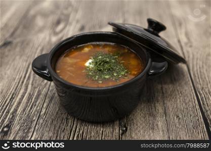 Tomato red pepper soup, sauce with olive oil, rosemary and smoked paprika in a beautiful ceramic pot on a wooden background.