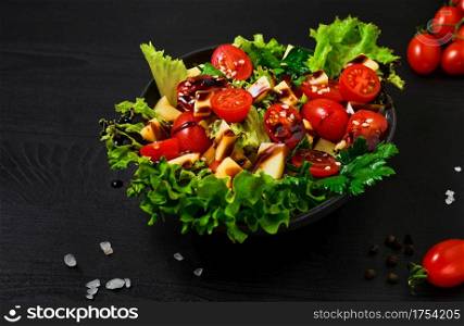 Tomato salad with lettuce, goat cheese, fresh vegetables, sesame seeds and olive oil on a black wooden table. Close-up. Healthy wholesome food