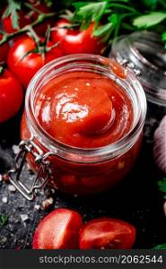 Tomato sauce in a glass jar with parsley and garlic. On a black background. High quality photo. Tomato sauce in a glass jar with parsley and garlic.