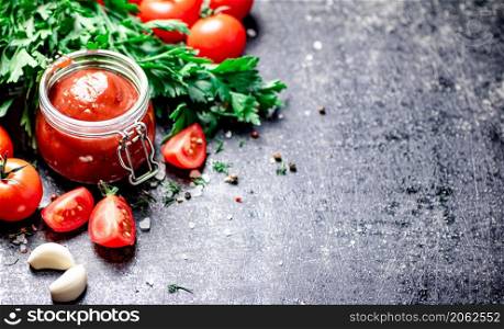 Tomato sauce in a glass jar with parsley and garlic. On a black background. High quality photo. Tomato sauce in a glass jar with parsley and garlic.