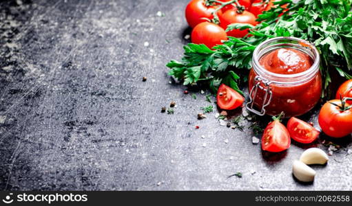 Tomato sauce in a glass jar with parsley and garlic. On a black background. High quality photo. Tomato sauce in a glass jar with parsley and garlic.