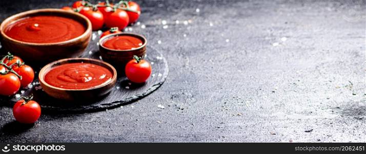 Tomato sauce in a wooden plate on a stone board with salt. On a black background. High quality photo. Tomato sauce in a wooden plate on a stone board with salt.