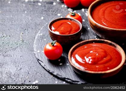 Tomato sauce in a wooden plate on a stone board with salt. On a black background. High quality photo. Tomato sauce in a wooden plate on a stone board with salt.