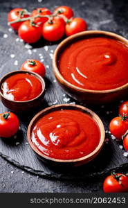 Tomato sauce in a wooden plate on a stone board with salt. On a black background. High quality photo. Tomato sauce in a wooden plate on a stone board with salt.