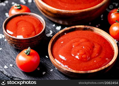 Tomato sauce in a wooden plate on a stone board with salt. On a black background. High quality photo. Tomato sauce in a wooden plate on a stone board with salt.