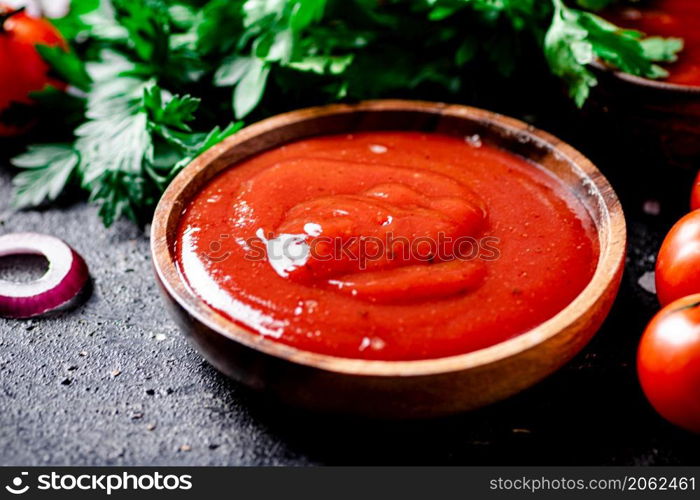 Tomato sauce in a wooden plate with onion rings and herbs. On a black background. High quality photo. Tomato sauce in a wooden plate with onion rings and herbs.