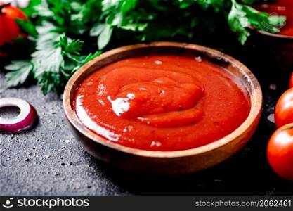 Tomato sauce in a wooden plate with onion rings and herbs. On a black background. High quality photo. Tomato sauce in a wooden plate with onion rings and herbs.