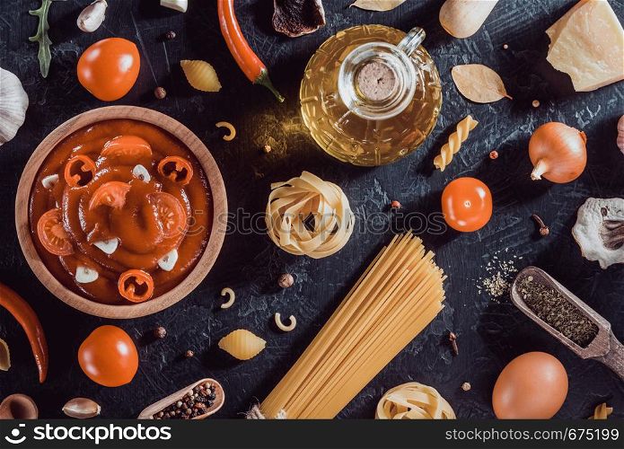 tomato sauce in bowl and pasta on black background table texture, top view