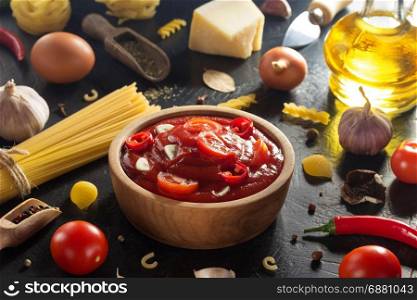 tomato sauce in bowl and pasta on black background texture