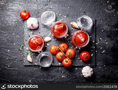 Tomato sauce in glass jars on a stone board with spices. On a black background. High quality photo. Tomato sauce in glass jars on a stone board with spices.