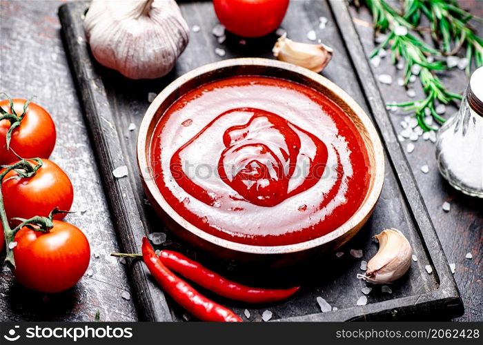 Tomato sauce on a cutting board with red pepper, garlic and rosemary. Against a dark background. High quality photo. Tomato sauce on a cutting board with red pepper, garlic and rosemary.