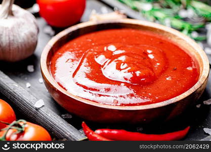 Tomato sauce on a cutting board with red pepper, garlic and rosemary. Against a dark background. High quality photo. Tomato sauce on a cutting board with red pepper, garlic and rosemary.