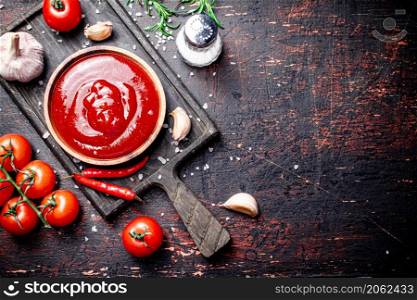 Tomato sauce on a cutting board with red pepper, garlic and rosemary. Against a dark background. High quality photo. Tomato sauce on a cutting board with red pepper, garlic and rosemary.