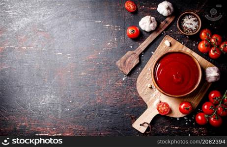 Tomato sauce on a wooden cutting board with garlic and spices. Against a dark background. High quality photo. Tomato sauce on a wooden cutting board with garlic and spices.