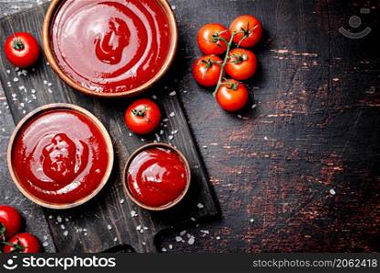 Tomato sauce on a wooden cutting board with pieces of salt. Against a dark background. High quality photo. Tomato sauce on a wooden cutting board with pieces of salt.
