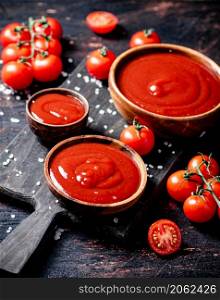 Tomato sauce on a wooden cutting board with pieces of salt. Against a dark background. High quality photo. Tomato sauce on a wooden cutting board with pieces of salt.