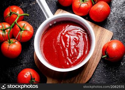 Tomato sauce with sauce roll on a wooden cutting board. On a black background. High quality photo. Tomato sauce with sauce roll on a wooden cutting board.