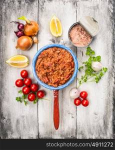 tomato sauce with tuna fish in old porridge pot and ingredient on white wooden background, top view