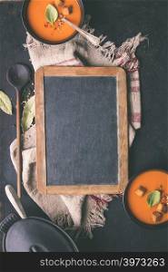 Tomato soup and fresh ingredients around vintage chalkboard on rustic background, top view, food frame, copyspace