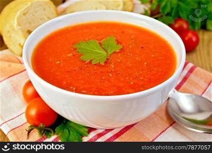 Tomato soup in a white bowl on a napkin, spoon, tomatoes, parsley, bread on a wooden boards background