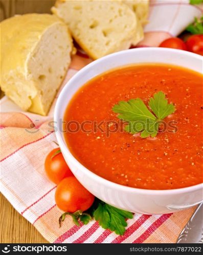 Tomato soup in a white bowl with a spoon on a napkin, tomatoes, parsley, bread on a wooden boards background